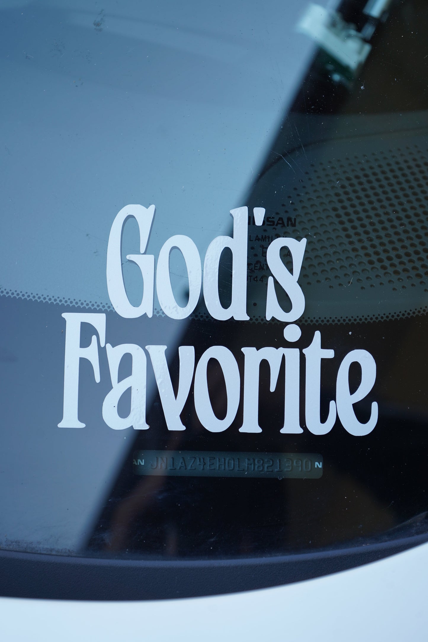 Close-up of a car window with 'God's Favorite' text in white on a reflective surface.