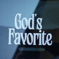 Close-up of a car window with 'God's Favorite' text in white on a reflective surface.